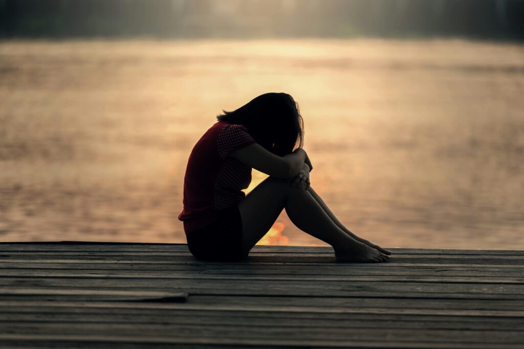 Overwhelmed woman sitting alone at sunset, illustrating the emotional weight of carrying the household mental load