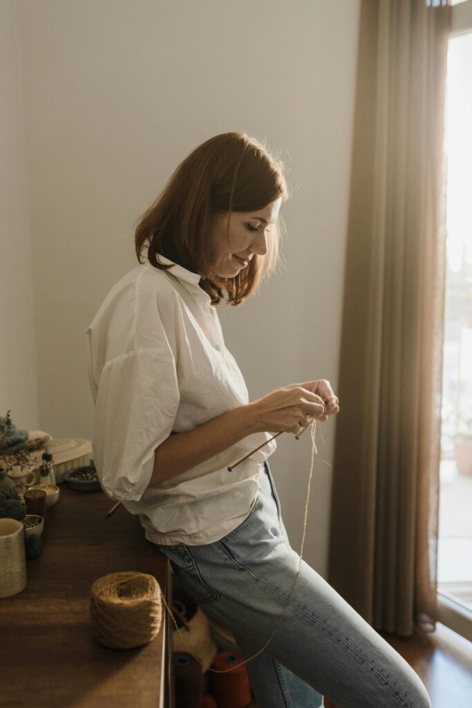 Woman sitting alone by a sunlit window, lost in thought — a quiet moment of self-reflection amid the mental load